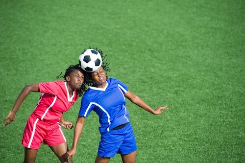 Two soccer players head the ball