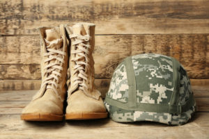 Pair of combat boots and military helmet on wooden background, close up